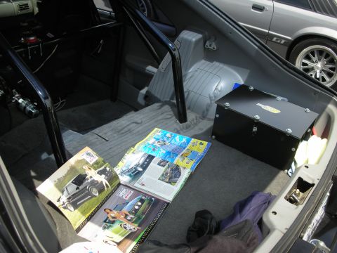 1992 Ford Crown Victoria - Magazines are open on the floor of a car's trunk, next to a black storage box and a roll cage.