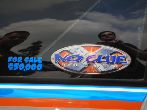 1992 Ford Crown Victoria - A car window displays a 'For Sale' sticker and a racing team decal, with reflections of people and clouds.