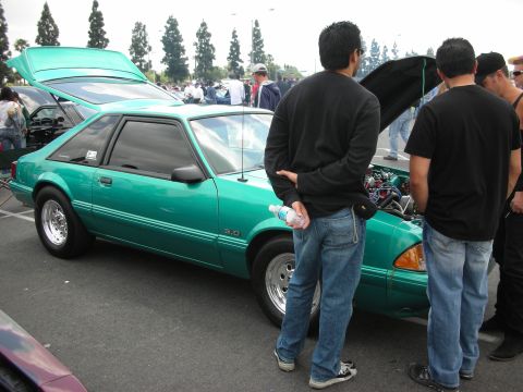 1992 Ford Crown Victoria - A green coupe with its hood open is displayed at an outdoor car show, with several people gathered around.