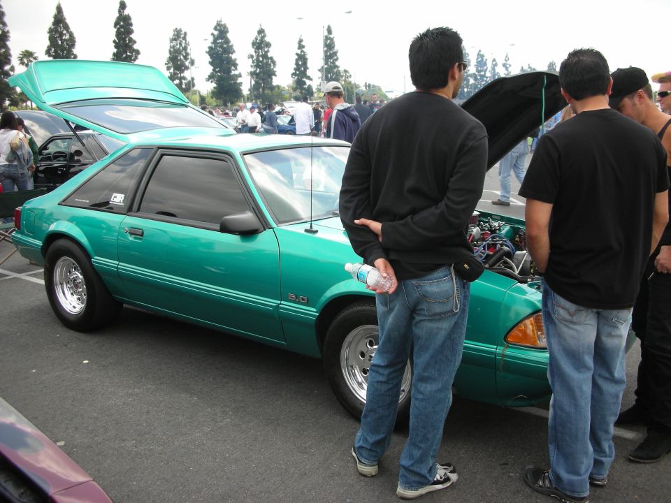 Green coupe with hood open, showing engine. "5.0" badge visible on fender