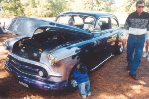 2002 Ford Crown Victoria - A man stands next to a heavily customized vintage sedan with its hood up, parked outdoors.