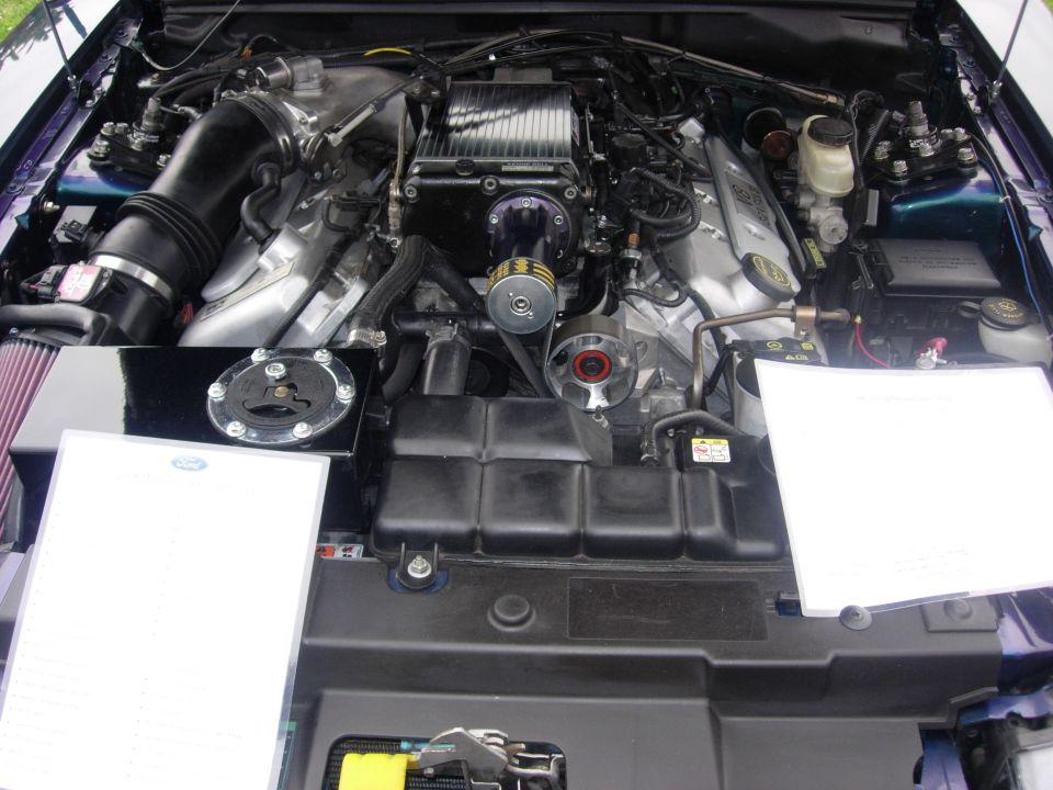 Engine bay with a supercharger, intake, and two white papers on display