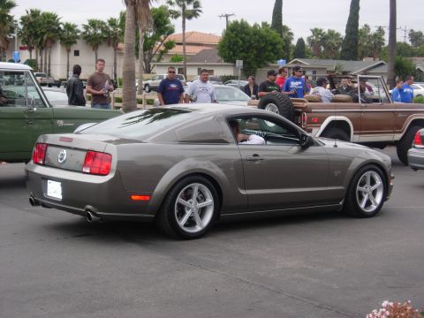 1992 Ford Crown Victoria - A gray Ford Mustang GT is seen from the rear quarter angle, parked among other vehicles and people.