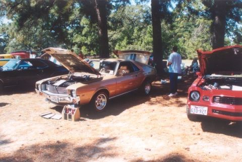 2002 Ford Crown Victoria - An orange AMC Javelin is displayed with its hood open, alongside other vehicles at an outdoor event.