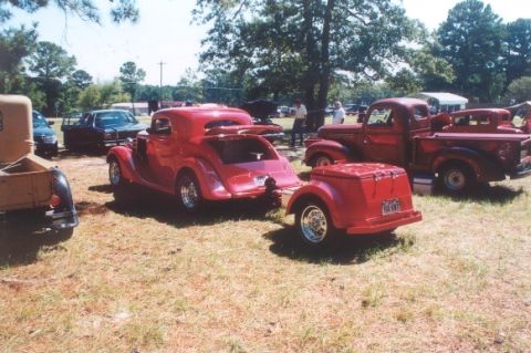 2002 Ford Crown Victoria - Several vintage vehicles, including a red coupe and trucks, are parked on a grassy field.