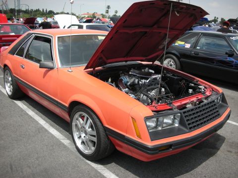1992 Ford Crown Victoria - This orange 1980s Ford Mustang coupe displays its engine and aftermarket wheels at a car show.