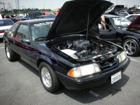 1992 Ford Crown Victoria - Black Ford Mustang with flame decals and custom wheels at a car show.