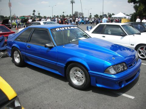 1992 Ford Crown Victoria - Custom blue coupe with a prominent hood scoop and 'OUTLAW' windshield banner at a car show.