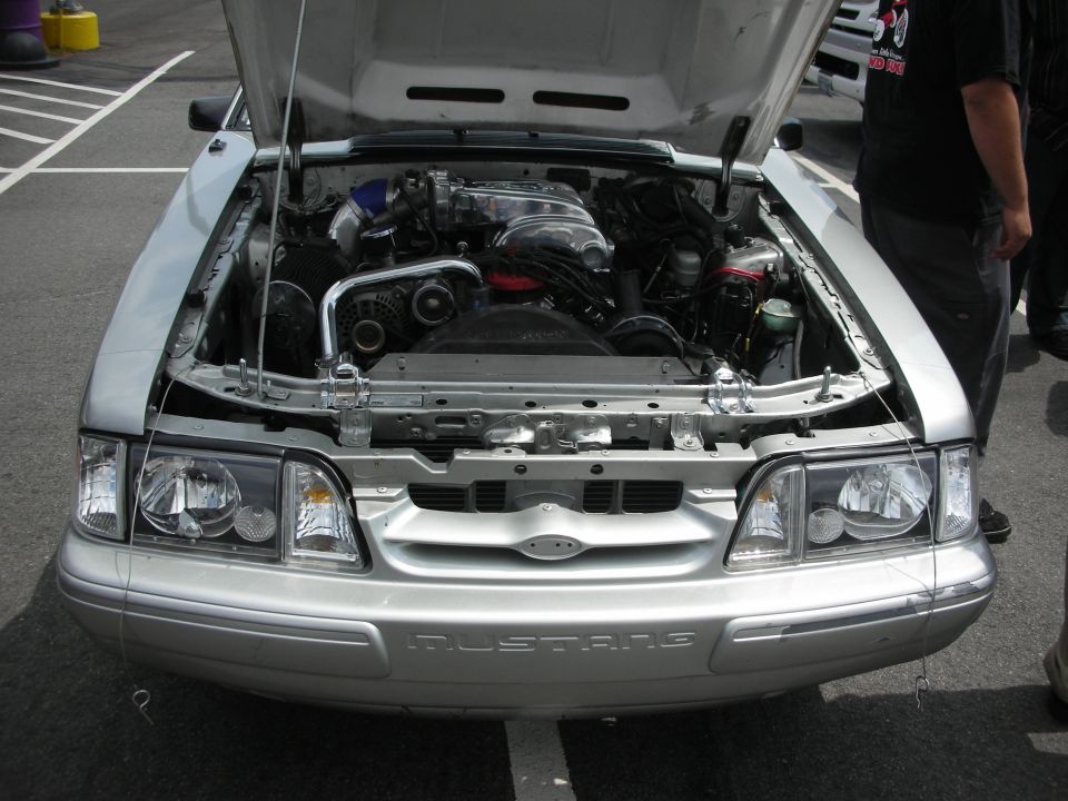 Silver Ford Mustang front view with engine exposed, "MUSTANG" text on bumper