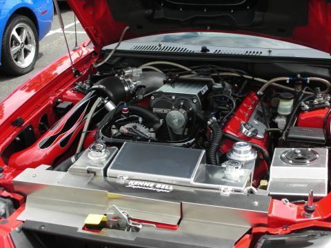 1992 Ford Crown Victoria - The engine bay of a red car is shown with a prominent supercharger and custom modifications, while another vehicle is partially visible.