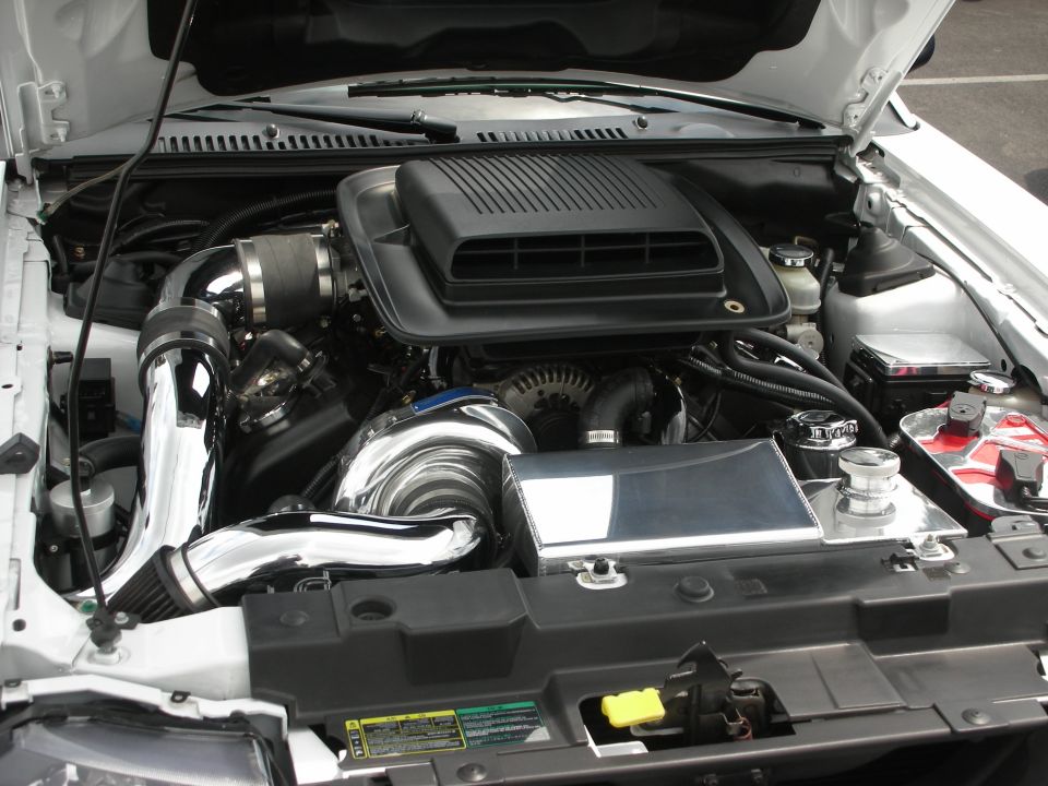 Engine bay with chrome turbocharger, intake piping, and black air intake. Hood is open
