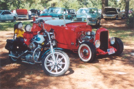 2002 Ford Crown Victoria - A motorcycle and a red hot rod car are parked outdoors with other vehicles in the background.