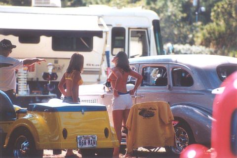 2002 Ford Crown Victoria - A vintage sedan is parked next to a yellow trailer, with two women standing nearby.