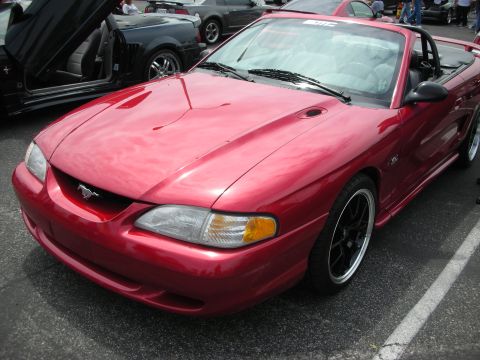 1992 Ford Crown Victoria - A red convertible sports car is parked in a lot next to other vehicles.
