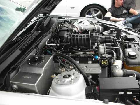 1992 Ford Crown Victoria - Close-up of a supercharged engine bay, with SVT branding visible on the engine cover. Another vehicle is partially visible in the backgroun…