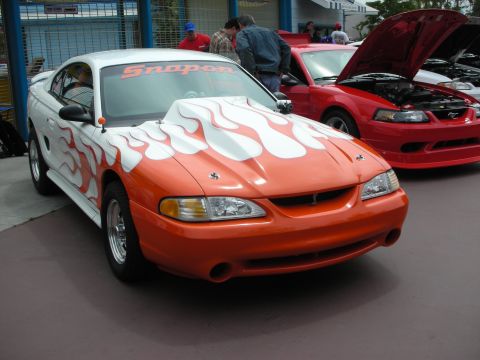 1992 Ford Crown Victoria - A customized Ford Mustang with flame graphics and a prominent hood scoop is displayed next to another Mustang with its hood open.