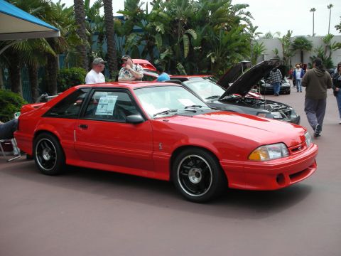 1992 Ford Crown Victoria - A red Ford Mustang is parked at an outdoor car show with other vehicles and people around.