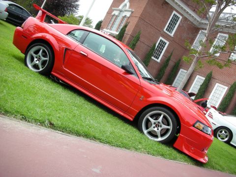 1992 Ford Crown Victoria - A red coupe with a prominent rear spoiler is displayed on a grassy lawn in front of a brick building.