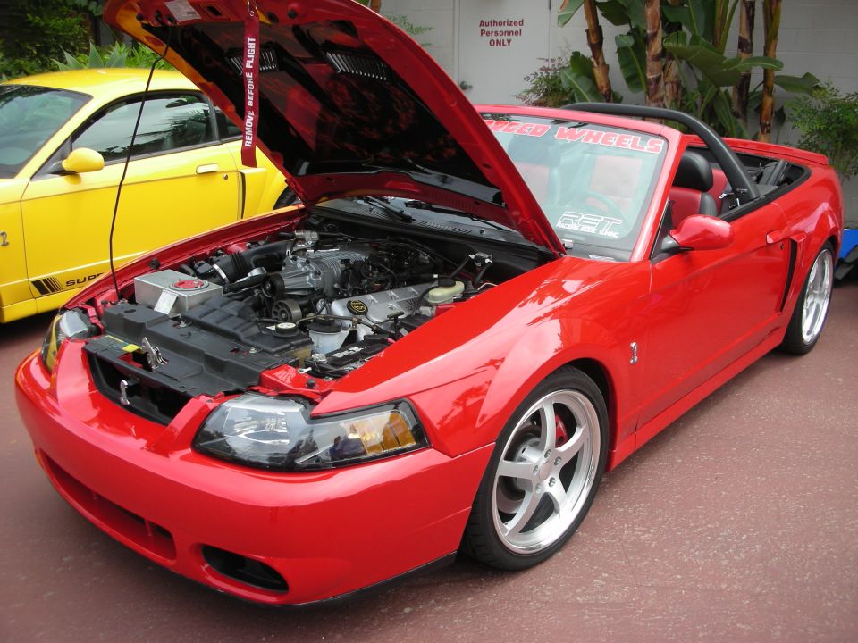 Red convertible with engine exposed, "BROAD WHEELS" sticker on windshield