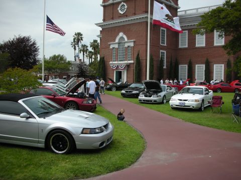 1992 Ford Crown Victoria - A car show multiple Ford Mustangs is held on the lawn in front of a historic brick building.