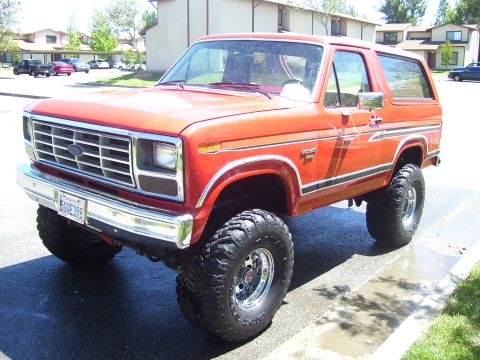 1986 Ford Bronco - Orange Ford Bronco with lifted suspension and off-road tires, parked on a street.