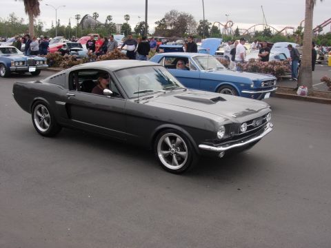 1992 Ford Crown Victoria - A dark gray 1965 Ford Mustang Fastback is parked at a car show with other vehicles present.