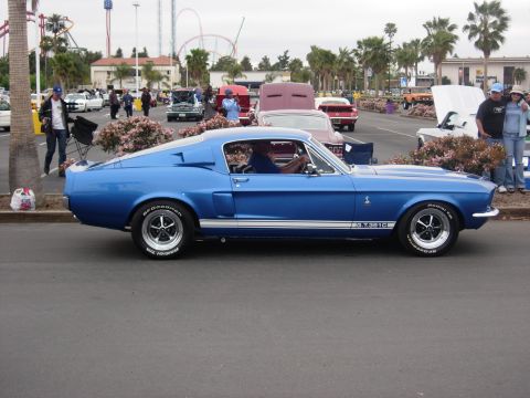 1992 Ford Crown Victoria - A blue 1967 Shelby GT350 fastback is parked at a car show with other vehicles visible in the background.