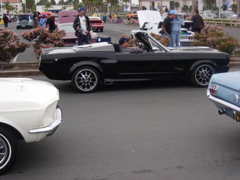 1992 Ford Crown Victoria - A black 1965 Ford Mustang convertible is parked at a car show with other classic vehicles.