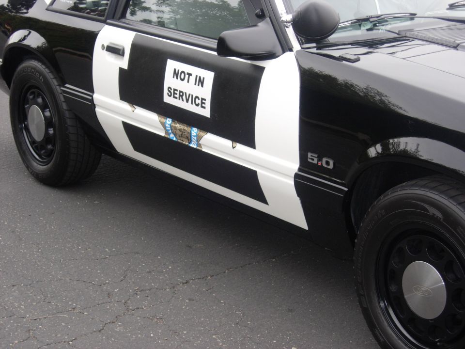 Black and white police car with "NOT IN SERVICE" text, 5.0 badge, and a damaged police crest