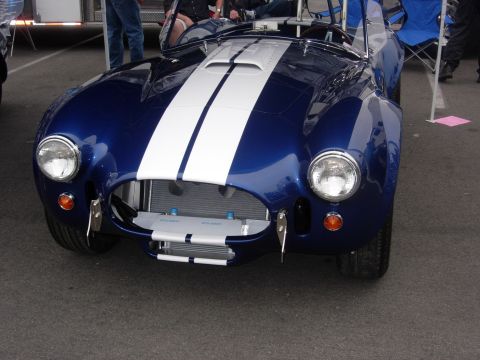 1992 Ford Crown Victoria - A blue AC Cobra replica with dual white racing stripes is parked on asphalt, with people and tents in the background.