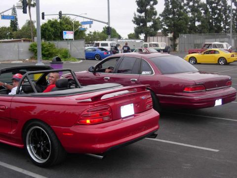 1992 Ford Crown Victoria - A maroon 1992 Ford Crown Victoria sedan is parked next to a red convertible.