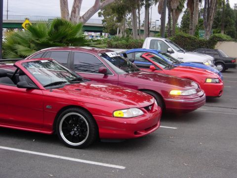 1992 Ford Crown Victoria - A line of cars, including a red convertible and a maroon sedan, are parked in a lot.