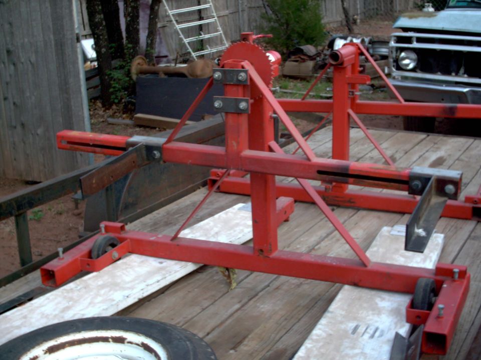 Red metal fabrication stands on a wooden trailer, with a spare tire in the foreground and a truck in the background