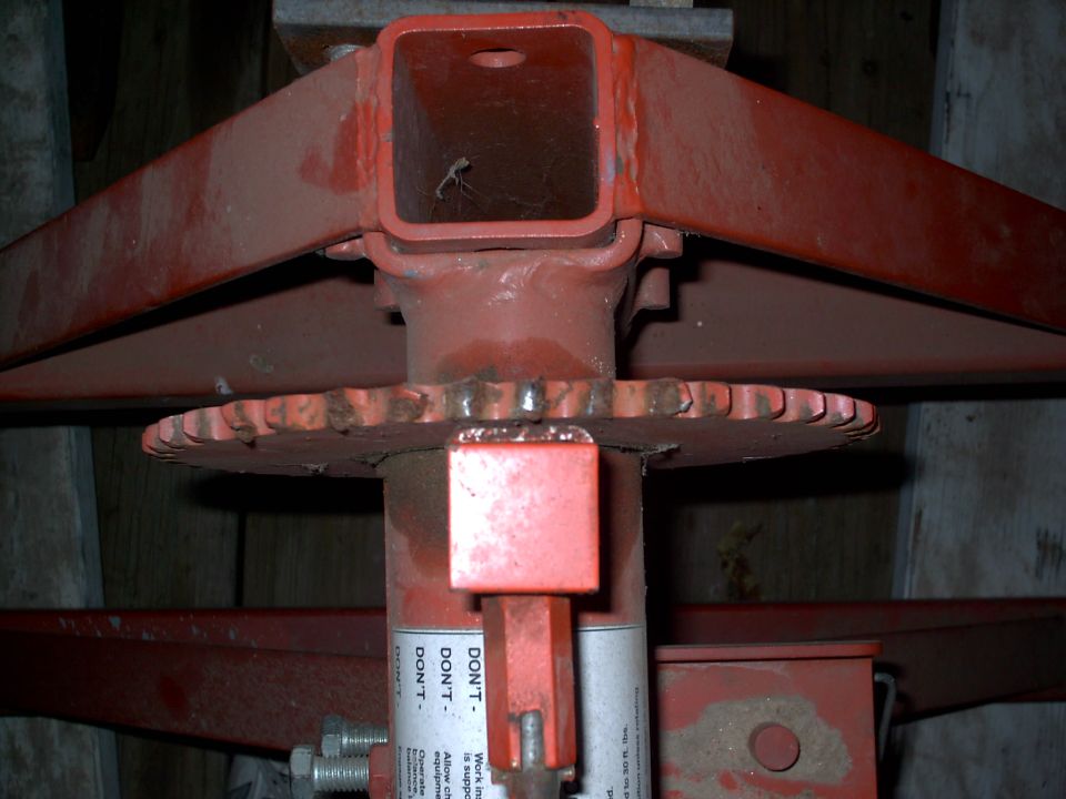 Close-up of a red metal jack mechanism with a toothed wheel and a warning label