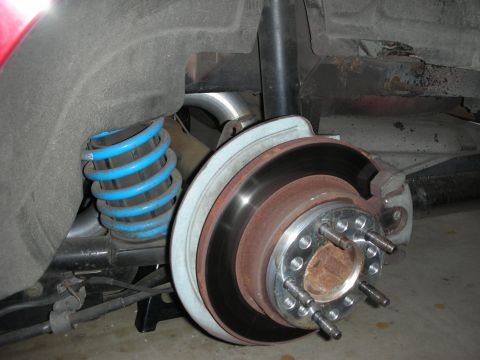 1998 Ford Crown Victoria - close-up of a vehicle's rear disc brake rotor, hub and lug studs alongside a bright blue lowering coil spring.