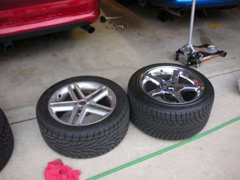 1998 Ford Crown Victoria - Two mounted wheels stand on a garage floor, one with a machined five-spoke face and one chrome five-spoke, with a jack in the background.