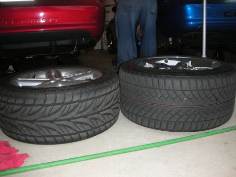 1998 Ford Crown Victoria - Two mounted wheels rest on a garage floor between a red and a blue car, a person in jeans standing behind them.