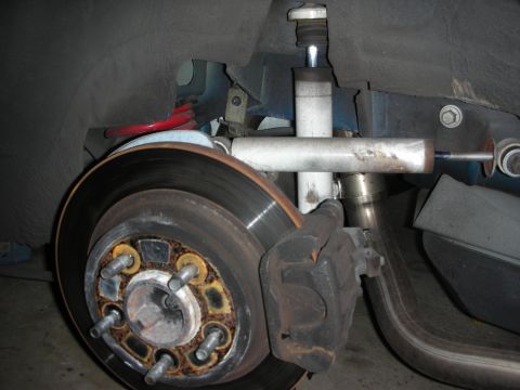 1998 Ford Crown Victoria - close-up of a front disc brake rotor, caliper and lug hub with surrounding suspension components on a lifted vehicle.