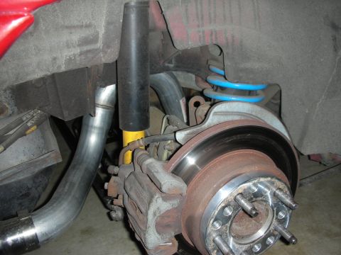 1998 Ford Crown Victoria - rear disc brake rotor and caliper sit beside a blue coil spring and yellow-bodied shock absorber under a red vehicle.