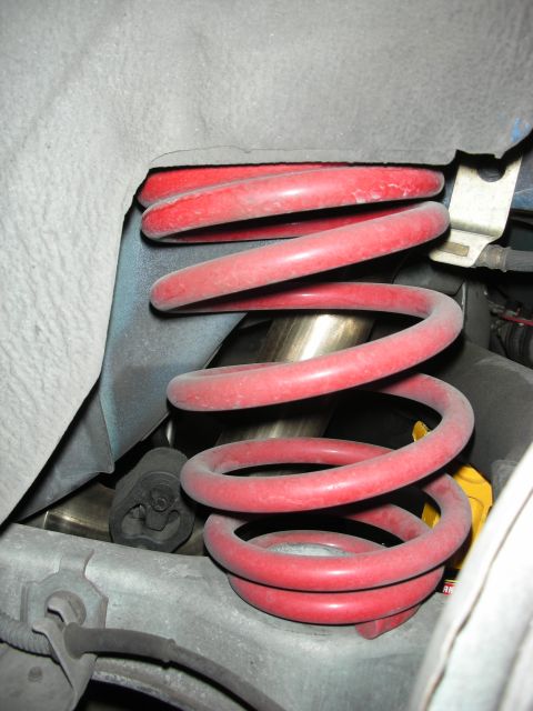 1998 Ford Crown Victoria - red-painted coil spring sits installed around a polished shock shaft within a vehicle's suspension tower.