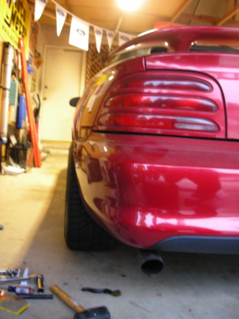 1998 Ford Crown Victoria - rear corner and taillight of a red Ford Mustang shine in a garage, with hand tools and a mallet scattered on the floor.