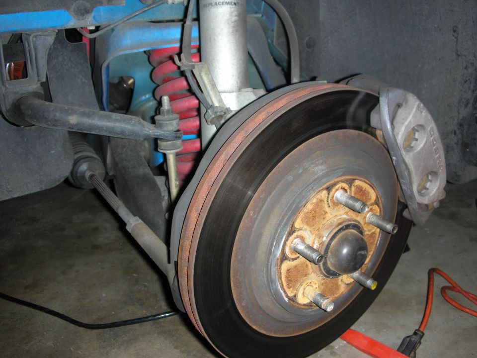 Rust-coated brake rotor and hub with red coil spring and suspension arms