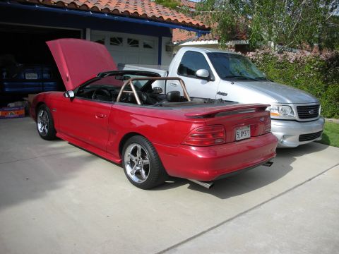 1998 Ford Crown Victoria - Rear three-quarter view of a red Mustang GT convertible with top down parked next to a silver Ford pickup in a driveway.