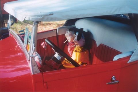 2002 Ford Crown Victoria - Two dolls are seated in the interior of a red vintage car, appearing to be passengers.
