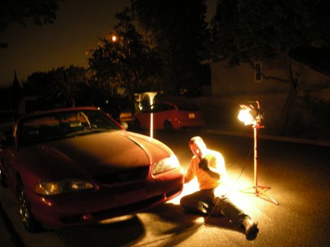 1998 Ford Crown Victoria - Nighttime driveway scene with a person in an orange shirt crouched beside a red convertible, illuminated by a portable work light.