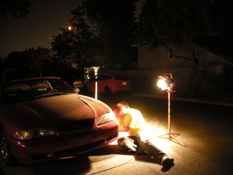 1998 Ford Crown Victoria - Nighttime scene of a person in an orange shirt seated near the front of a red convertible, lit by a tripod work light.