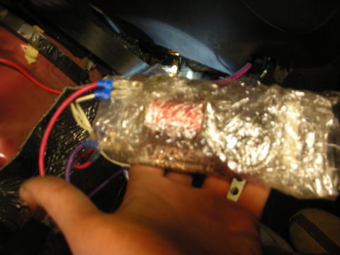 1998 Ford Crown Victoria - hand holds a plastic-wrapped audio crossover with red windings near exposed car wiring with blue and white connectors.