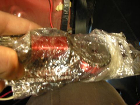 1998 Ford Crown Victoria - Close-up of a hand holding a plastic-wrapped Kicker audio crossover showing a red coil winding, inside a vehicle.