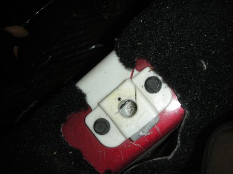 1998 Ford Crown Victoria - white plastic terminal block with metal studs mounted in a cutout of black carpet over a red painted panel.