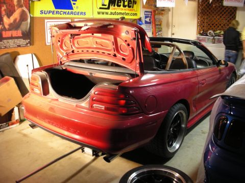 1998 Ford Crown Victoria - Rear-quarter view of a red Mustang convertible with the trunk open in a shop, surrounded by Superchargers and AutoMeter banners.